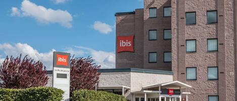 A modern hotel with a prominent 'ibis' sign, a brick facade, and a covered entrance.