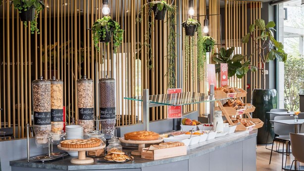 Um buffet de café da manhã com diversos alimentos, incluindo pães e um bolo, e um espaço com café, uma máquina de café e xícaras.