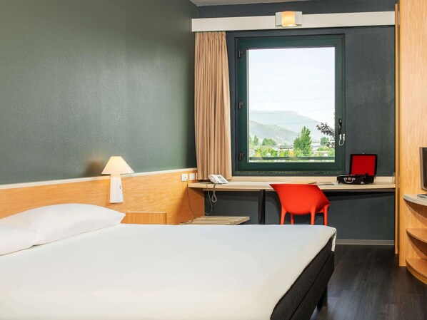A hotel room with a bed, desk, chair, and a window with a view. - ibis Firenze Prato Est (Campi Bisenzio)