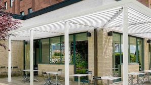 An outdoor seating area with tables and chairs, a covered section with glass walls, and 'ibis' signage on the building. - ibis Firenze Prato Est (Campi Bisenzio)