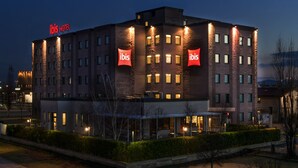 Um hotel com vários andares, com a sinalização 'ibis', fachada bem iluminada e área frontal ajardinada.