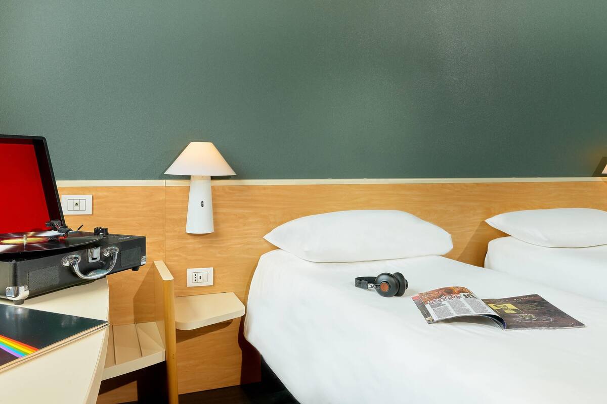 Ett hotellrum med en sÀng, ett skrivbord med en bÀrbar dator, en lampa och en tidning.
