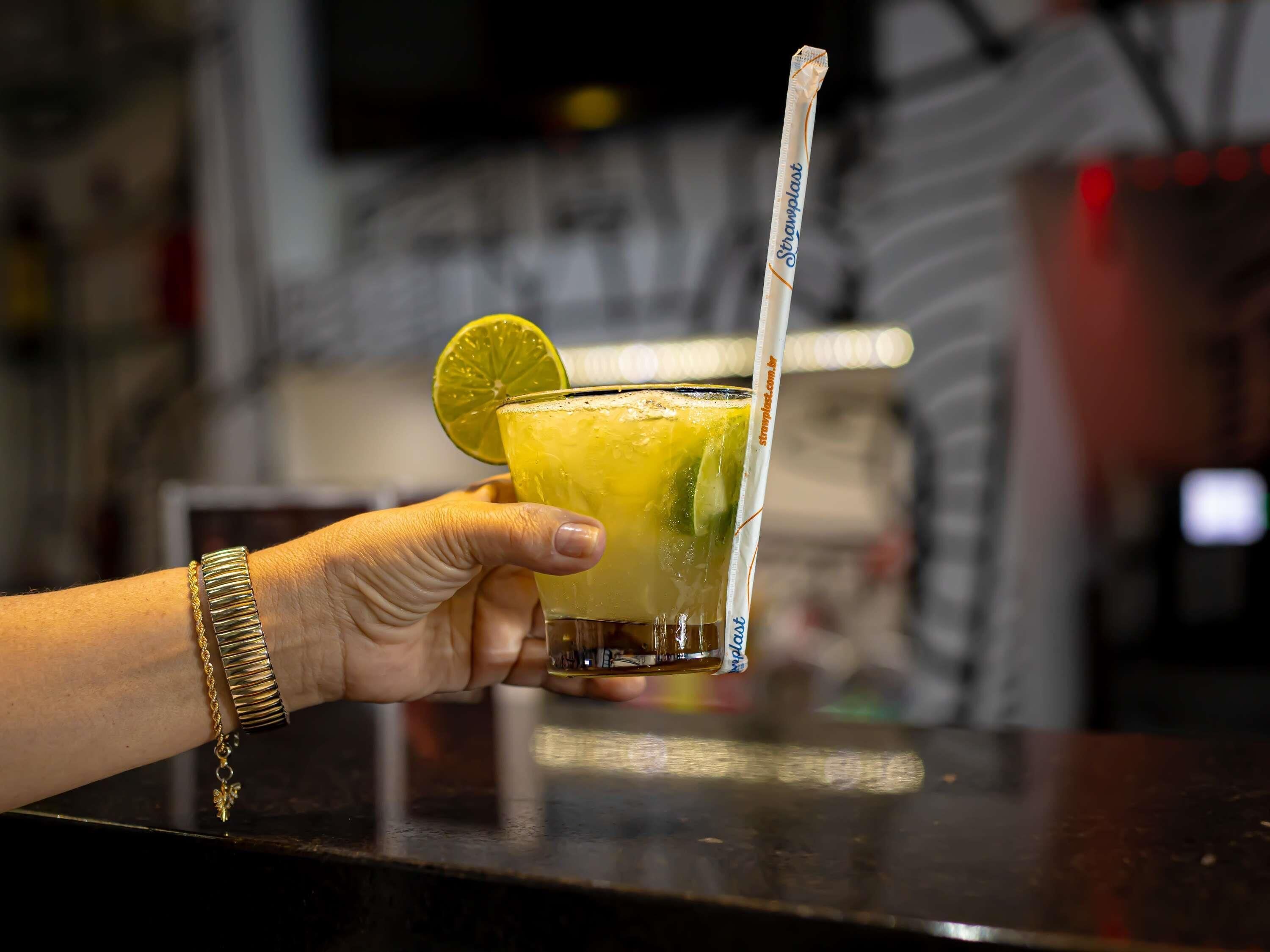 A hand holding a glass with a straw, garnished with a lime slice, on a bar counter.