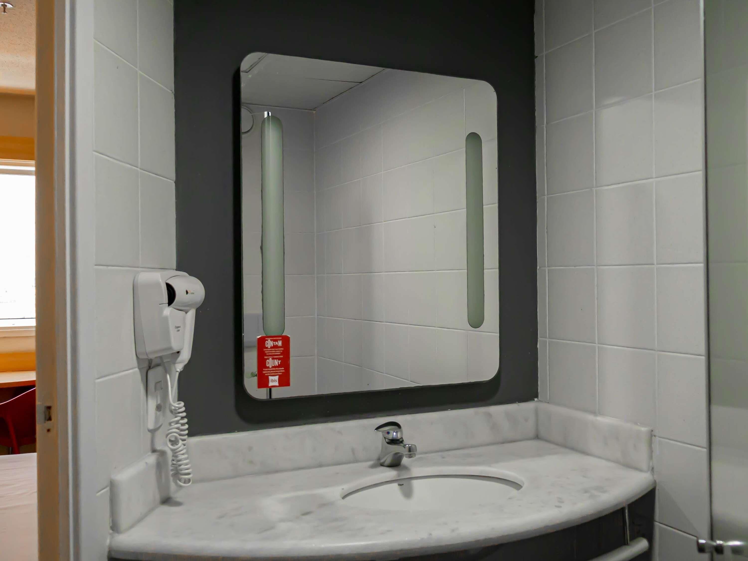 Un baño con un lavabo blanco, un espejo y un secador de manos.