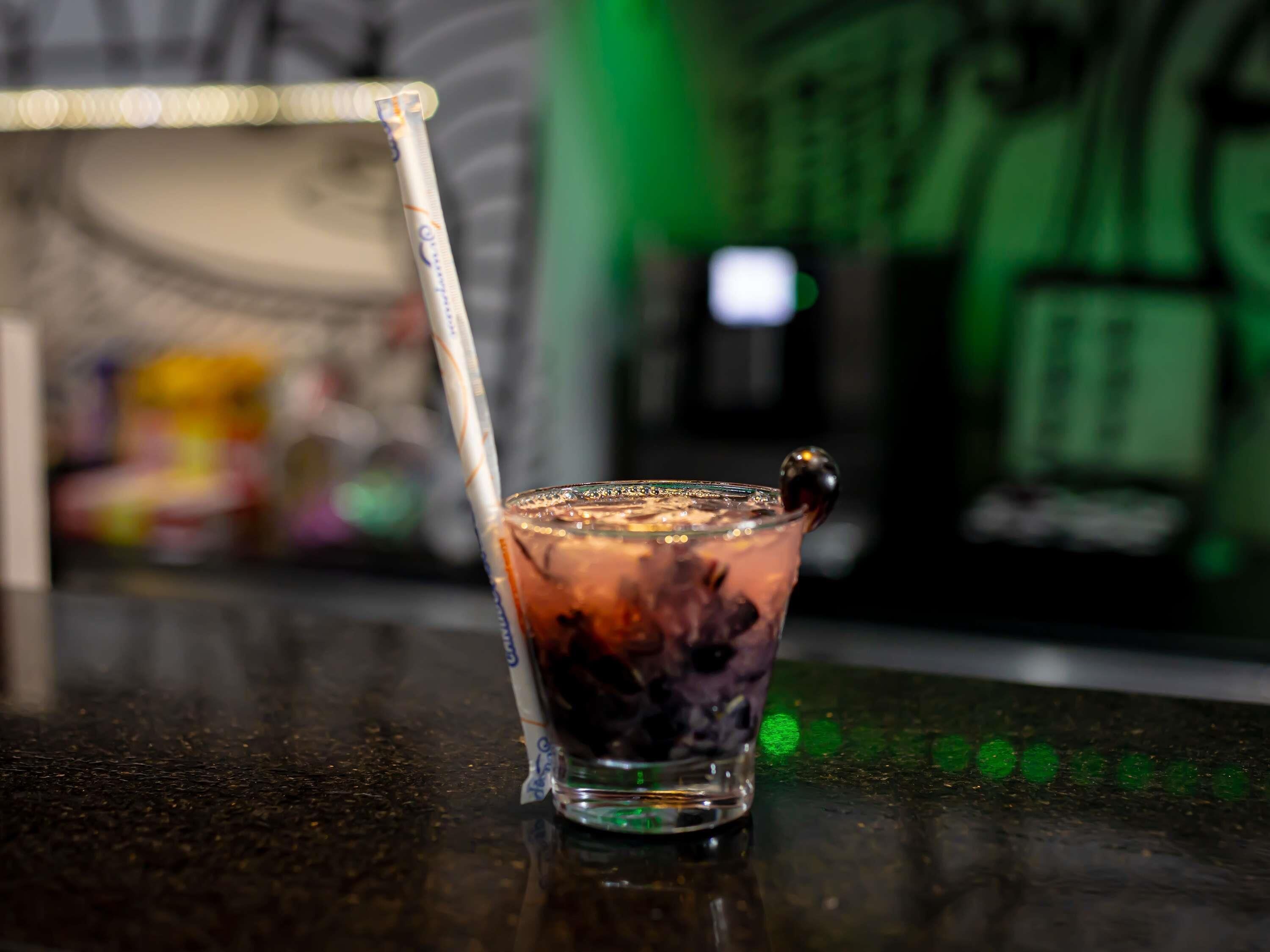A glass of iced beverage with a straw, placed on a reflective surface.