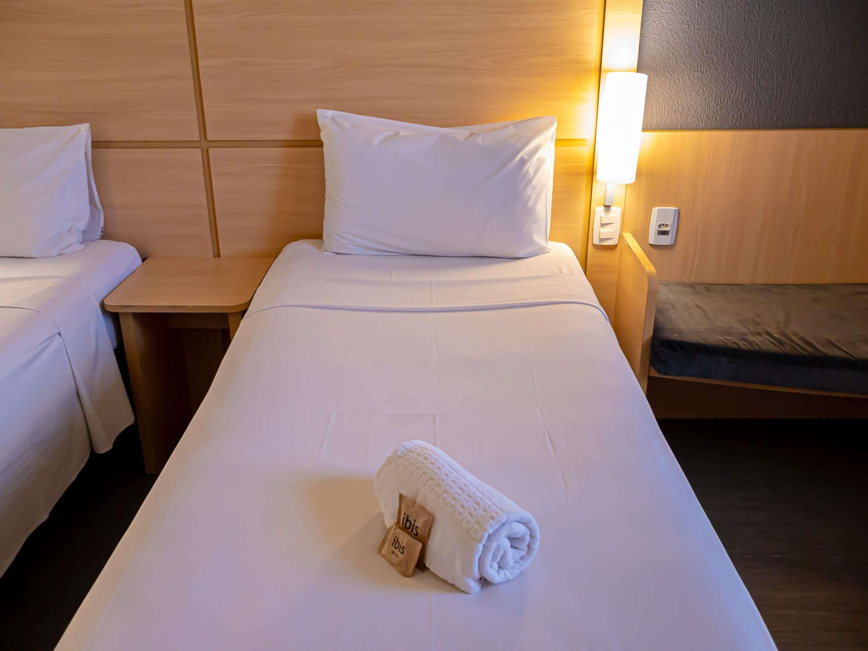 Une chambre d’hôtel avec deux lits, une tête de lit en bois, une lampe de chevet et une serviette roulée posée sur le lit.