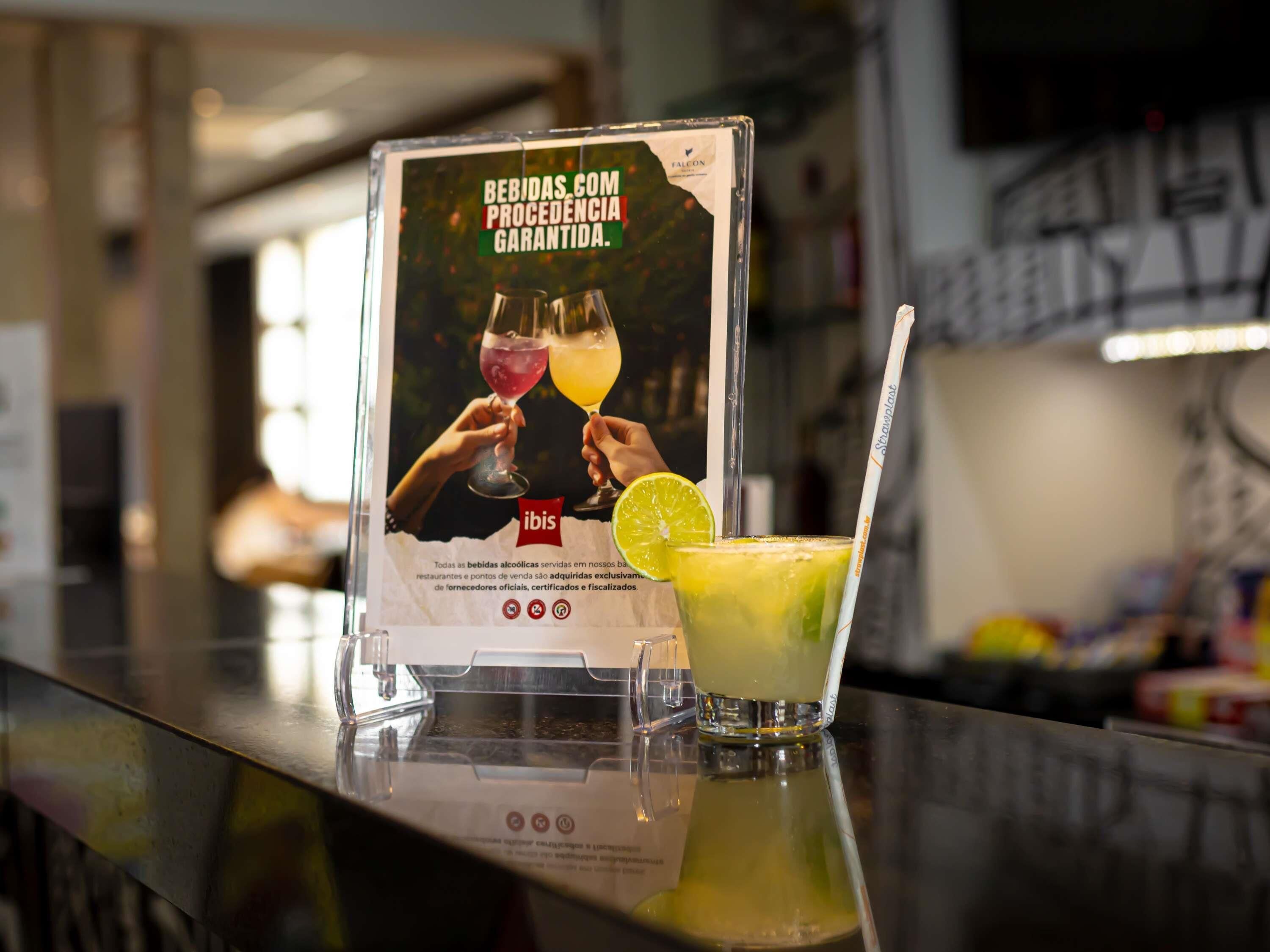 Eine Bar mit Werbeschild für Getränke, ein Glas grüner Cocktail mit Limettenscheibe und einem Strohhalm.