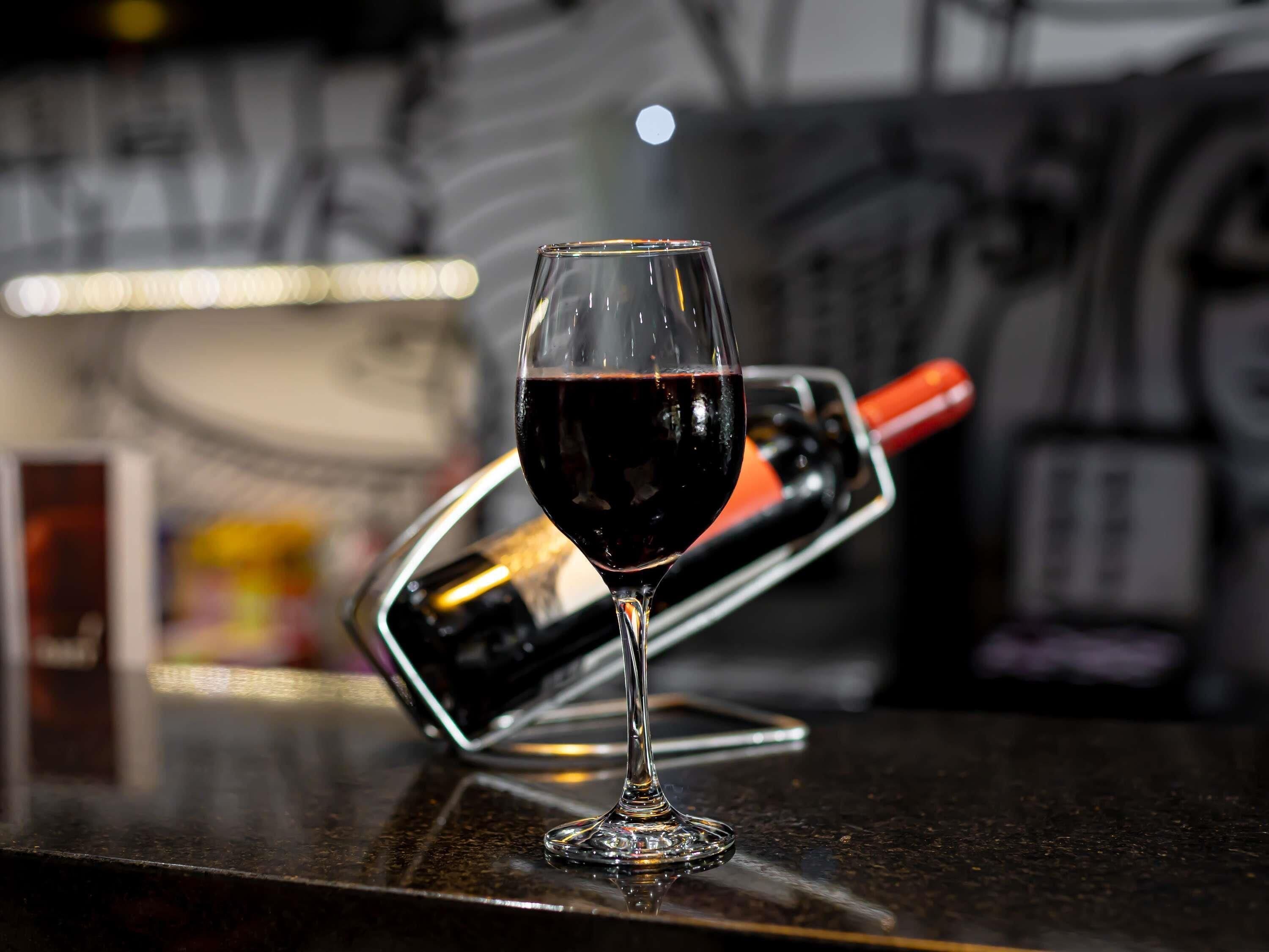 A wine glass filled with red wine on a bar counter with a wine bottle opener in the background.