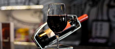 A wine glass filled with red wine on a bar counter with a wine bottle opener in the background.