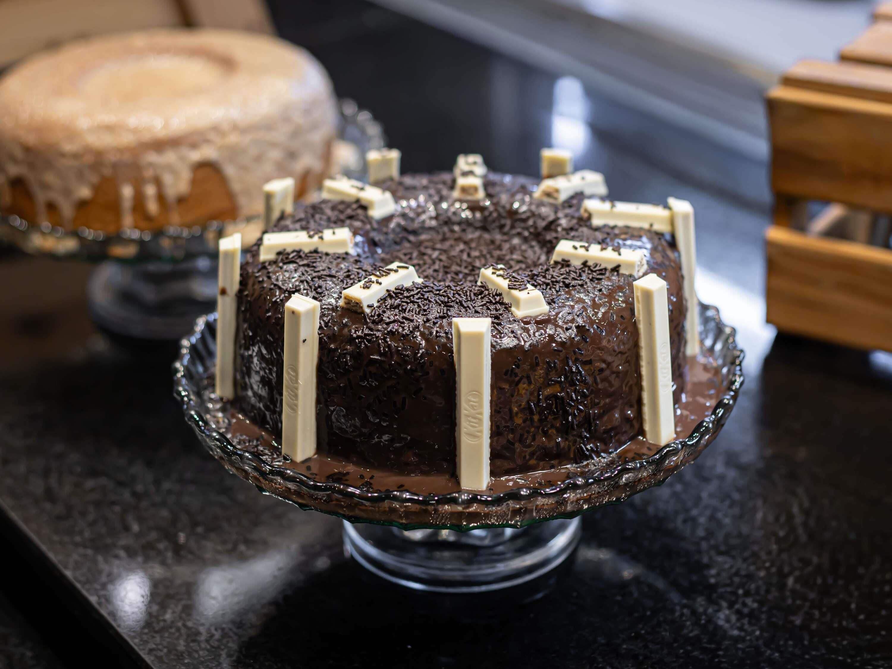 A chocolate cake with white chocolate sticks on a glass cake stand.