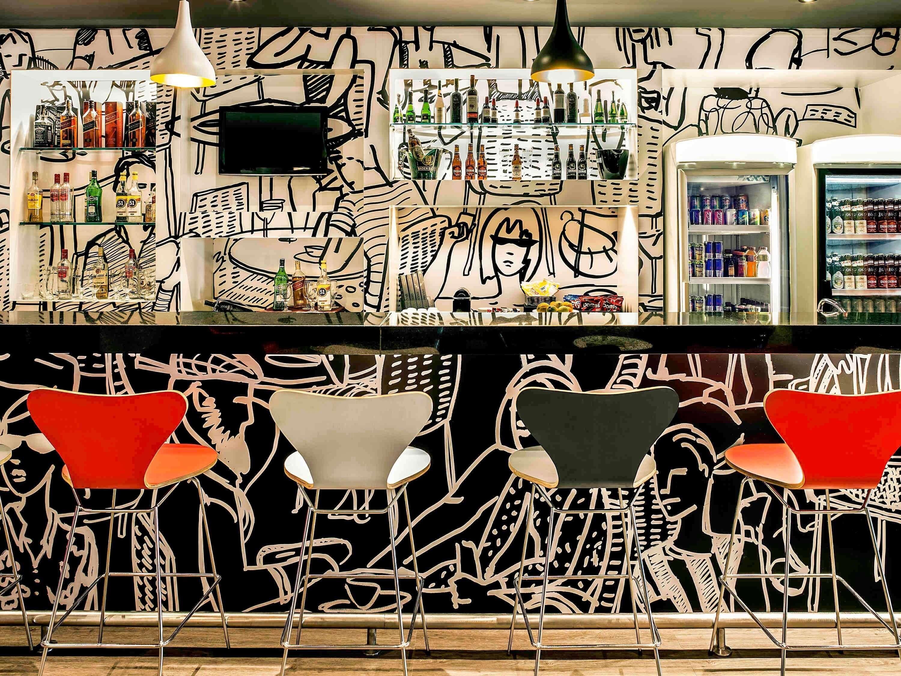 A bar area with graffiti art, shelves of liquor, and red chairs.