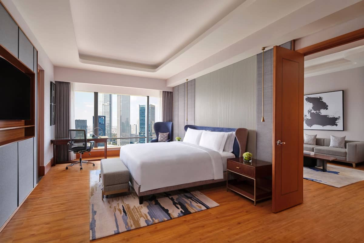 A modern hotel room with a large bed, a desk, and a view of the city skyline.