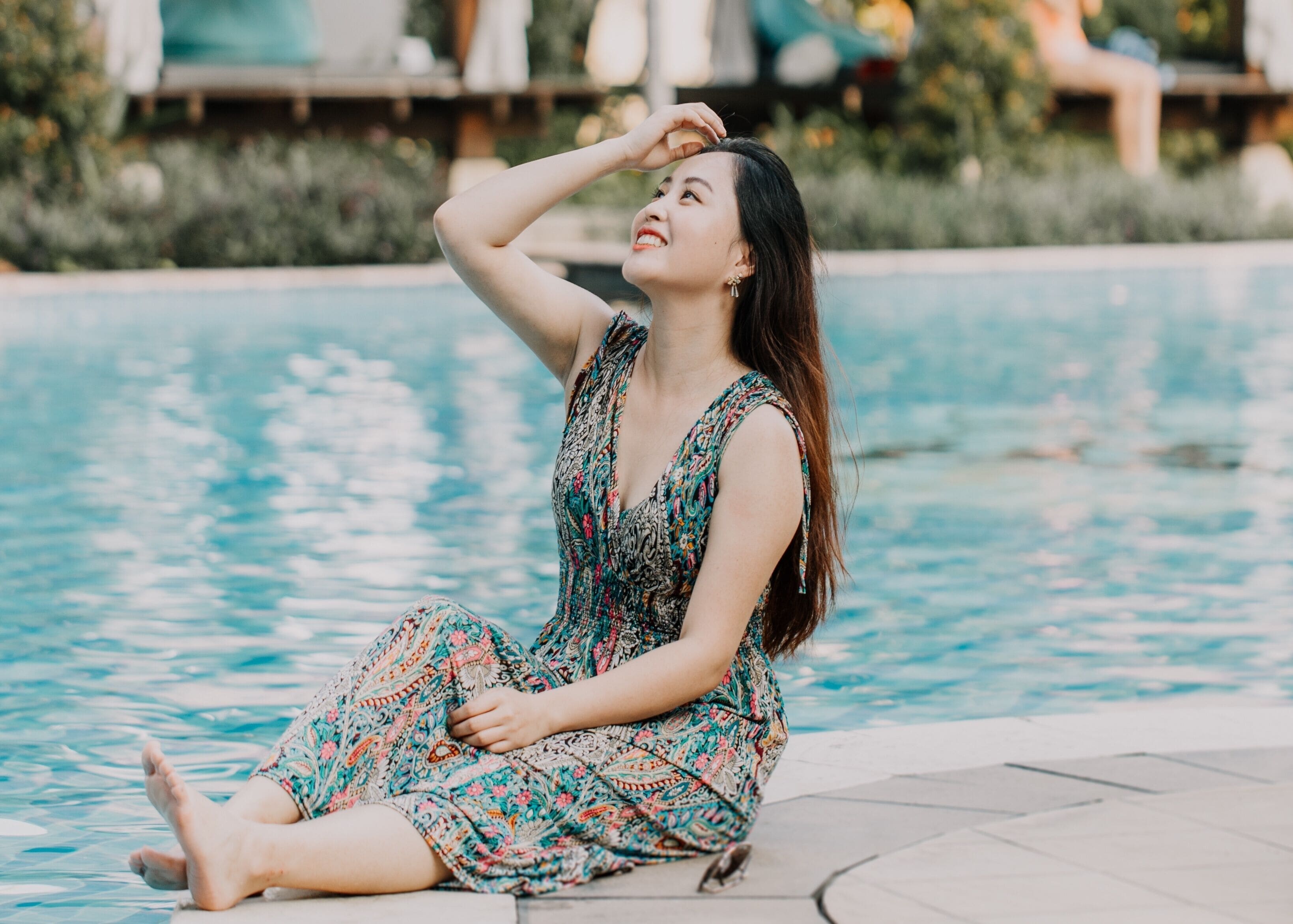 Una persona sentada junto a una piscina con un vestido estampado.
