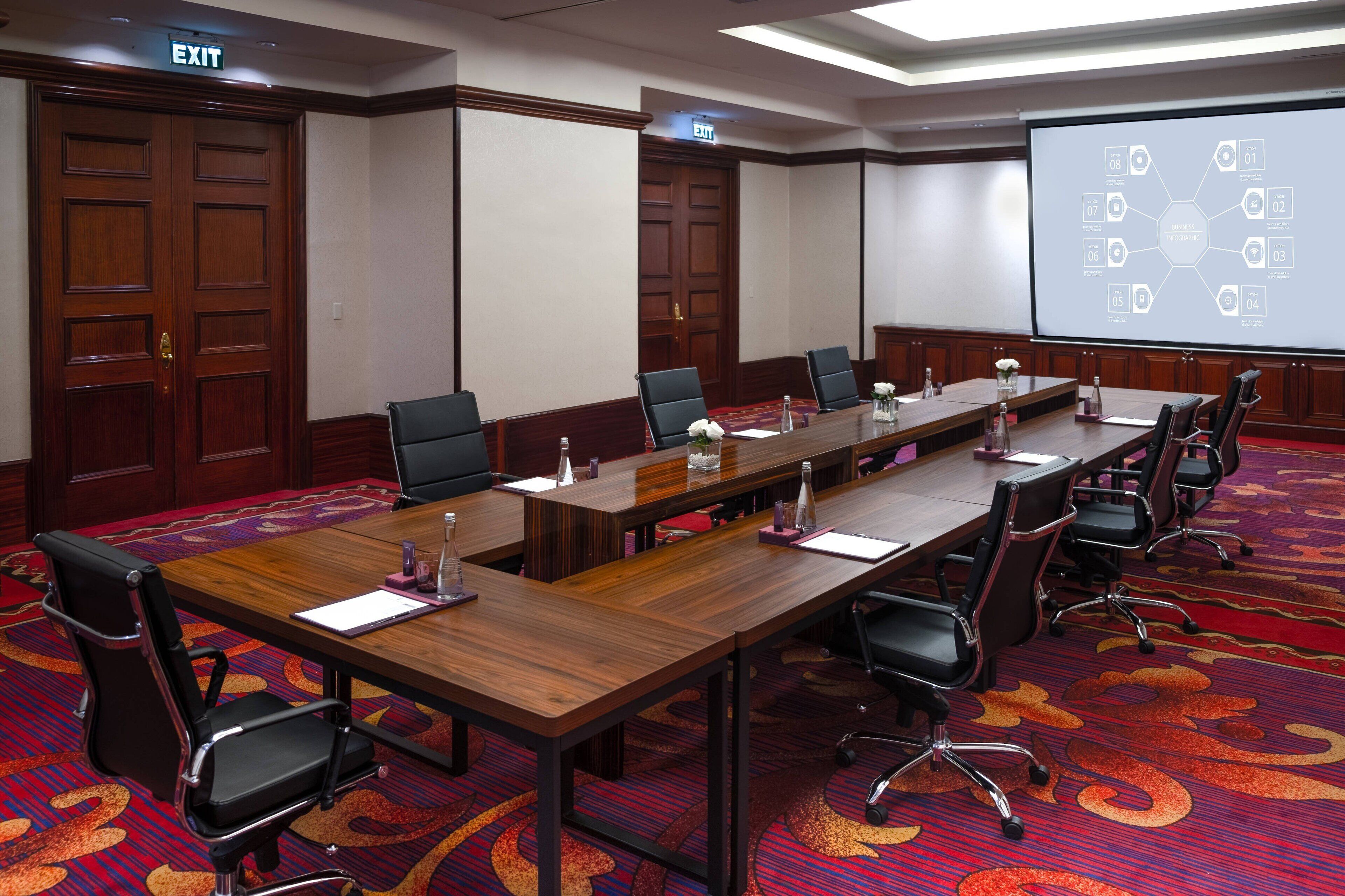 A conference room with a long table, multiple chairs, and a projector screen displaying a presentation.