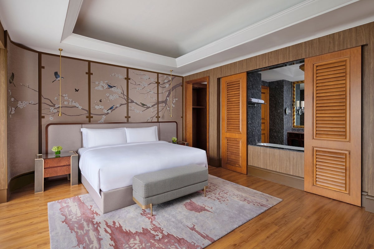 A modern bedroom with a large bed, a bedside table, a bench, a wall-mounted TV, and a wardrobe with sliding doors.