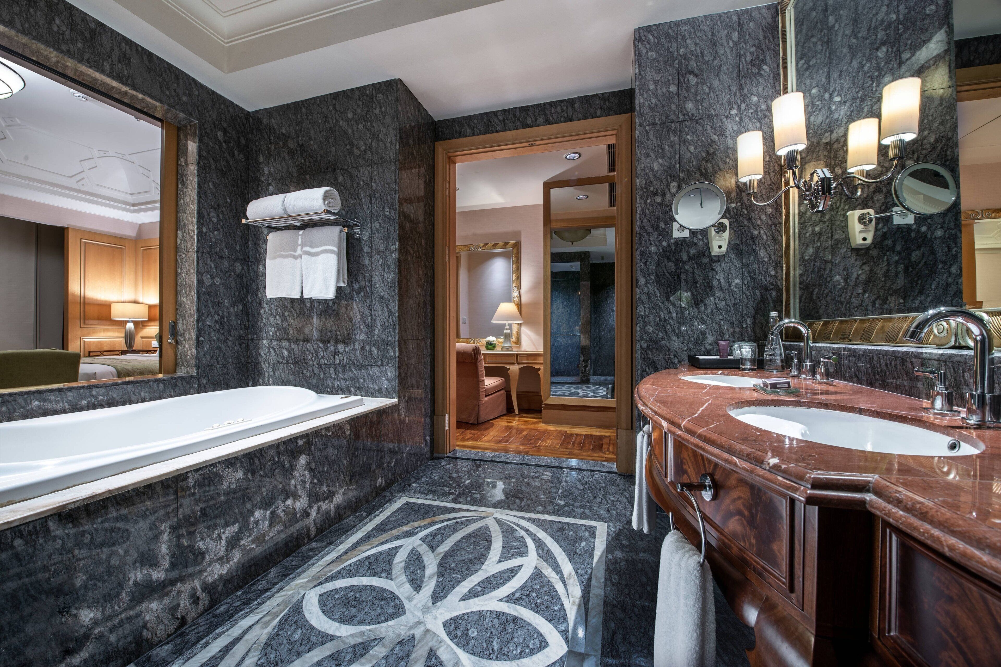 A modern bathroom with a large bathtub, two sinks, and a mirror with lights.