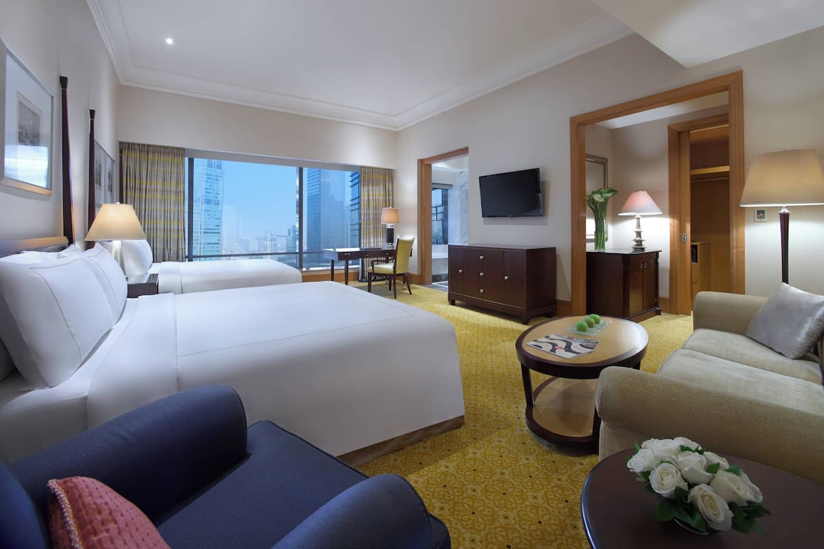 A hotel room with two beds, a sofa, a dining table, and a TV.