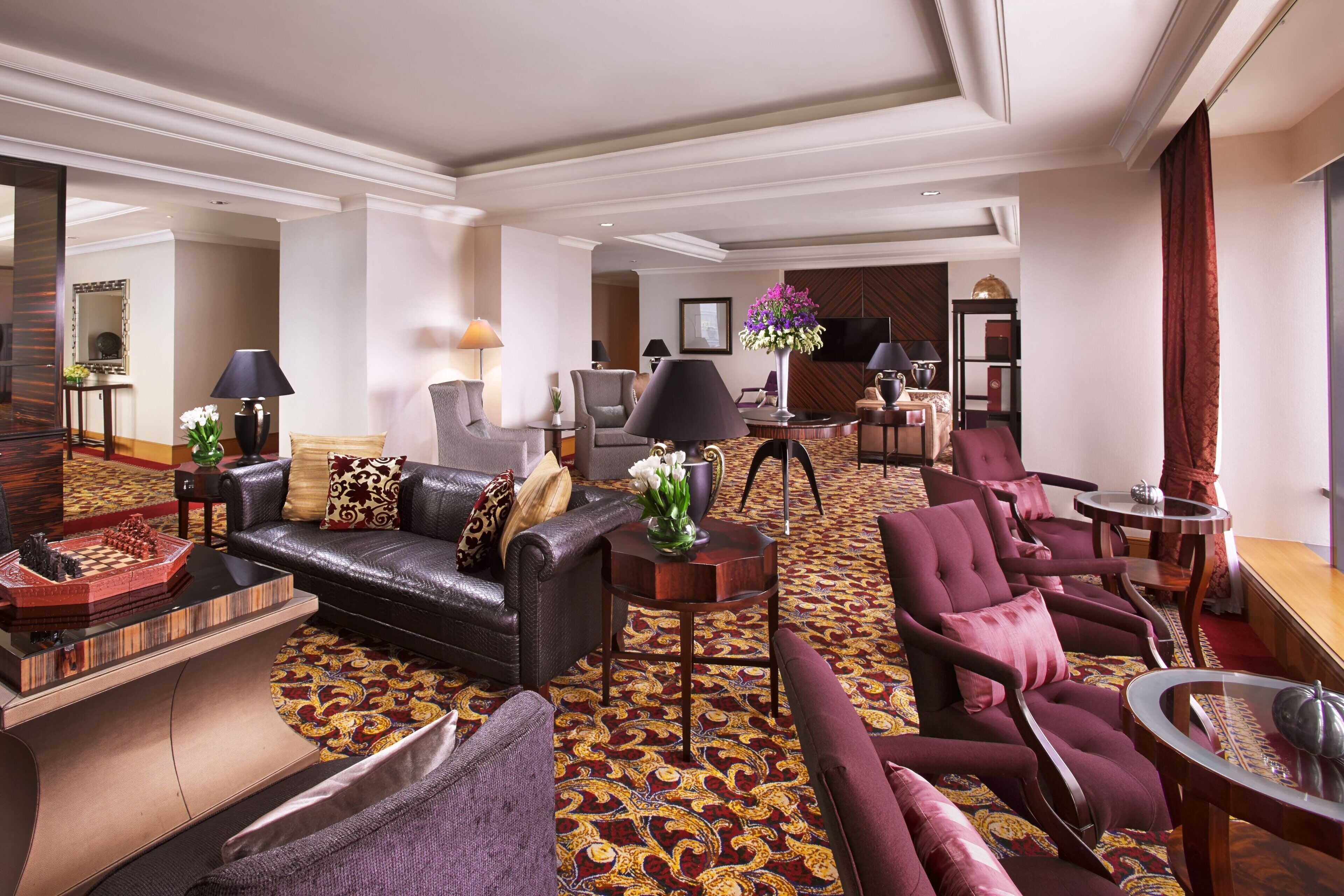 A spacious living area with a black leather sofa, multiple armchairs, a coffee table, and a patterned carpet.