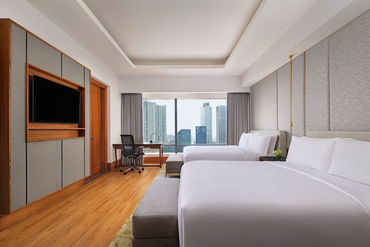 A hotel room with two beds, a desk, a chair, and a TV.