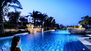 A swimming pool with clear blue water, surrounded by palm trees and stone structures.