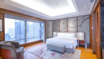 A modern bedroom with a large bed, a seating area, and a city view.