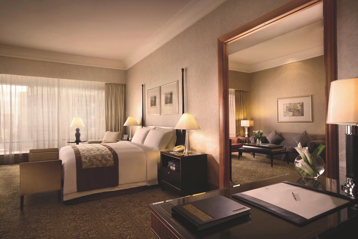 A hotel room with a large bed, two bedside tables with lamps, a desk with a chair, a mirror, and a view of the city through the window.