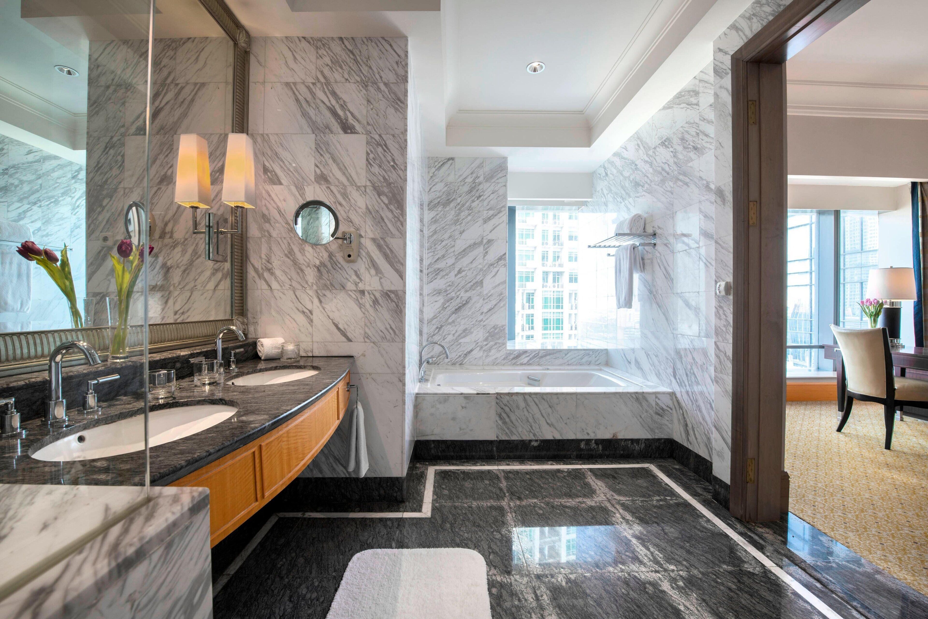 A modern bathroom with two sinks, a large mirror, and a bathtub.