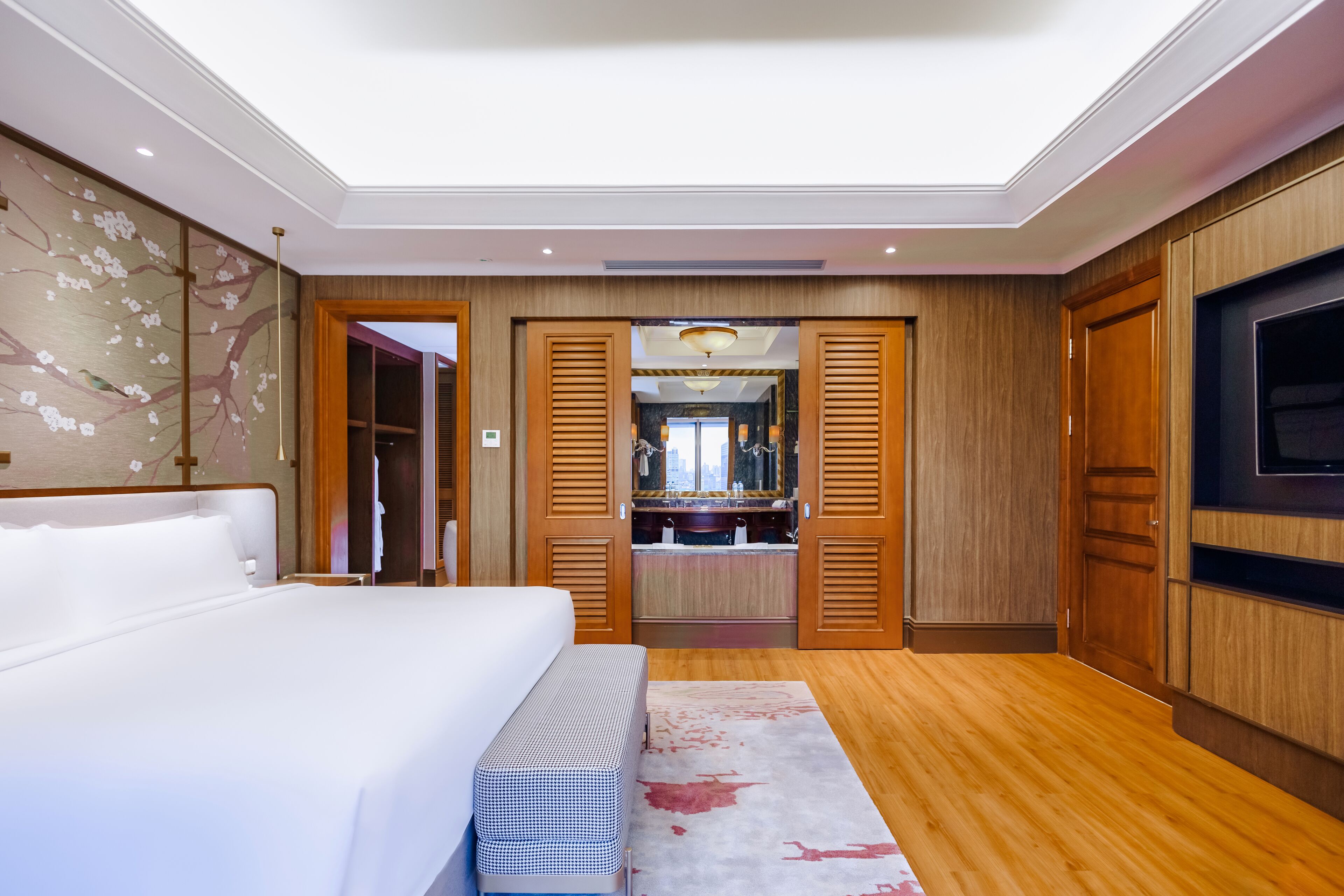 A modern hotel room with a large bed, wooden wardrobe, and a TV.