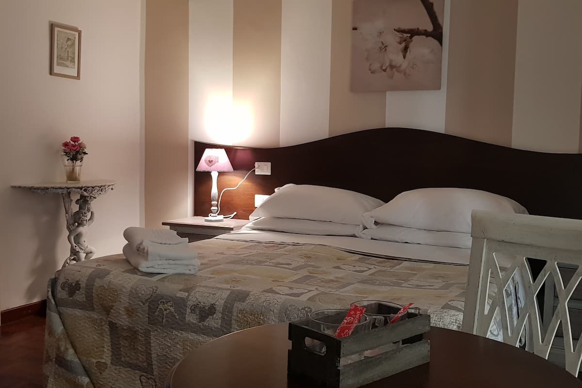 Een hotelkamer met een bed, nachtkastje, lamp en een stoel.