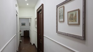 A narrow hallway with white walls, wooden doors, and framed artwork on the walls. - Napoli Centrale (Naples)