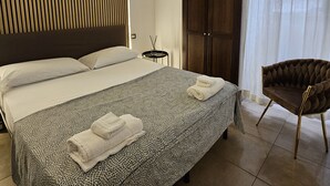 A modern bedroom with a large bed, a wooden slat wall, an air conditioning unit, a dark wooden wardrobe, and a chair. - Napoli Centrale (Naples)