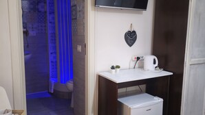 A compact room with a small kitchenette, a flat-screen TV mounted on the wall, a heart-shaped decoration, and a small refrigerator. - Napoli Centrale (Naples)