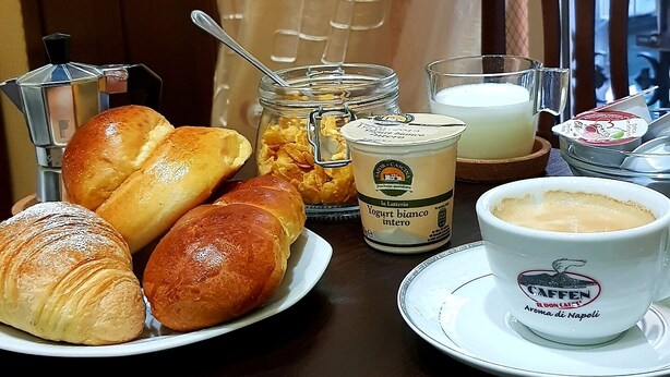 A breakfast table with croissants, a coffee pot, a jar of yogurt, and a cup of coffee. - Napoli Centrale (Naples)