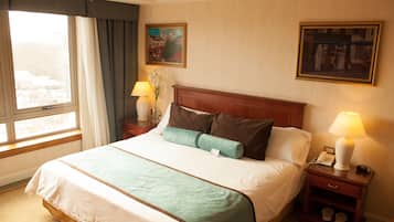 A hotel room with a large bed, two bedside tables, a nightstand, a window with curtains, and two framed pictures on the wall.