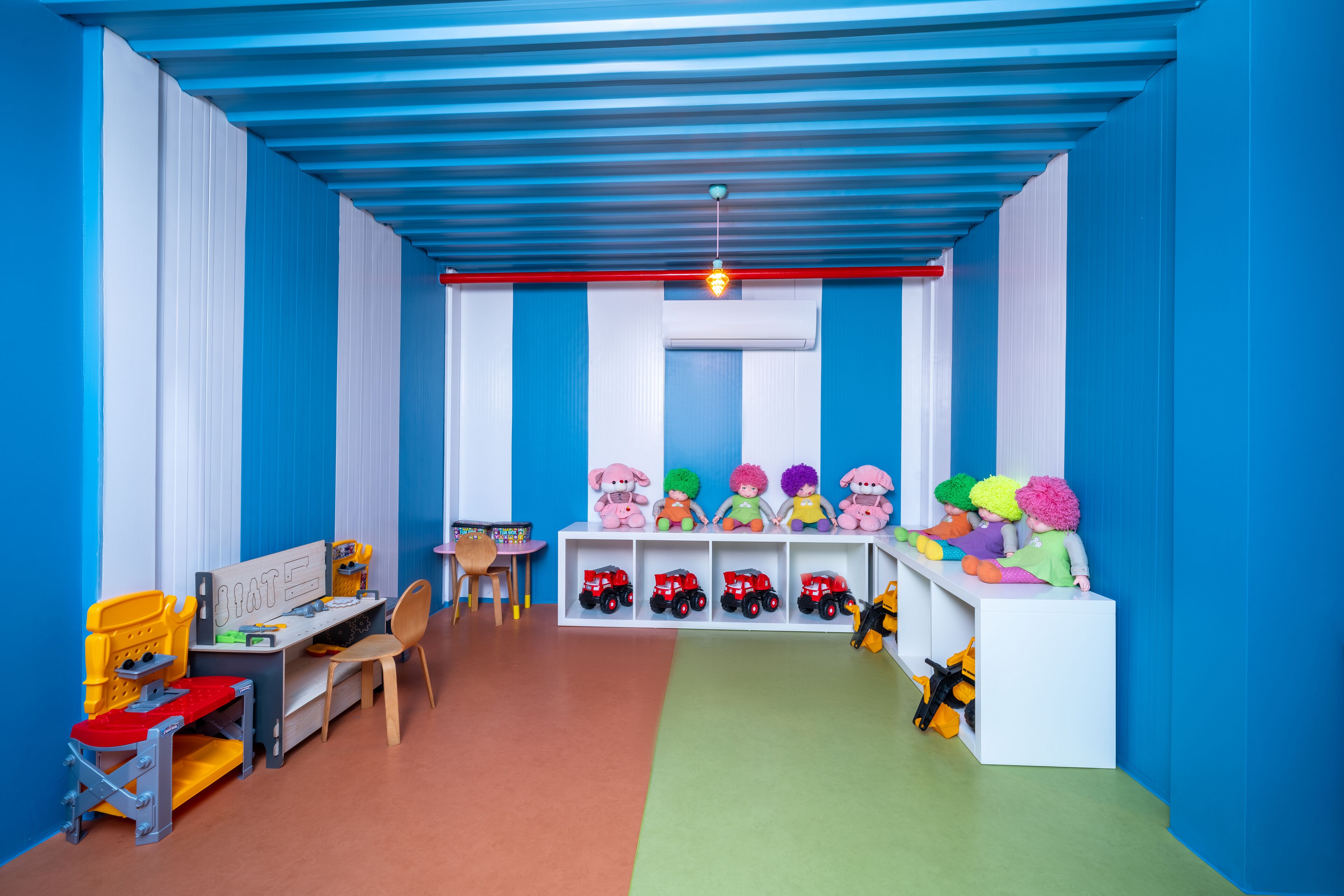 A children's playroom with a blue and white color scheme, featuring a desk, chairs, shelves with toys, and a play area with toy vehicles.