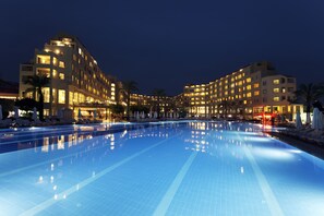 A hotel with a swimming pool, multiple floors, and a well-lit facade at night.