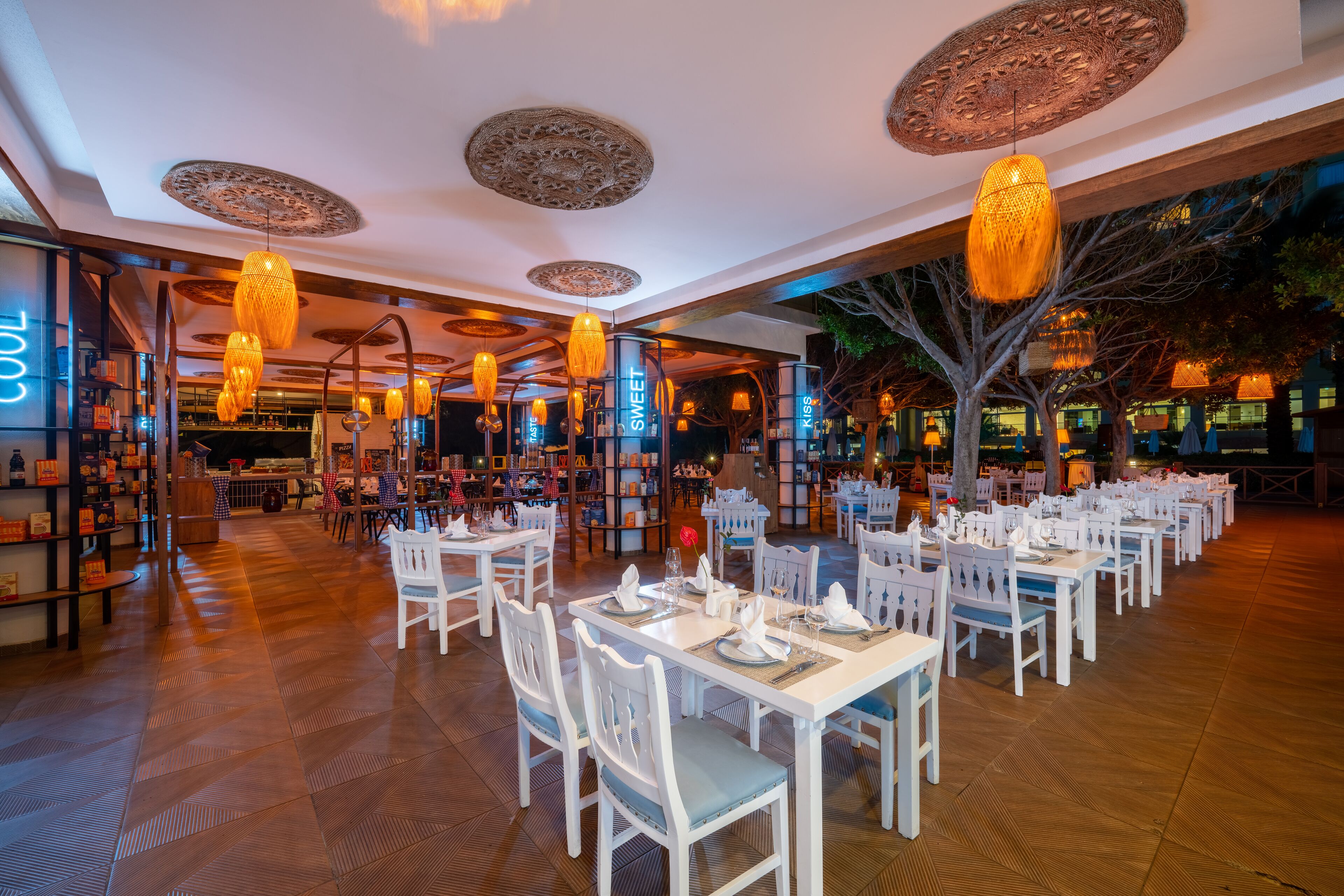 A restaurant with white tables and chairs, hanging lamps, and a patterned ceiling.