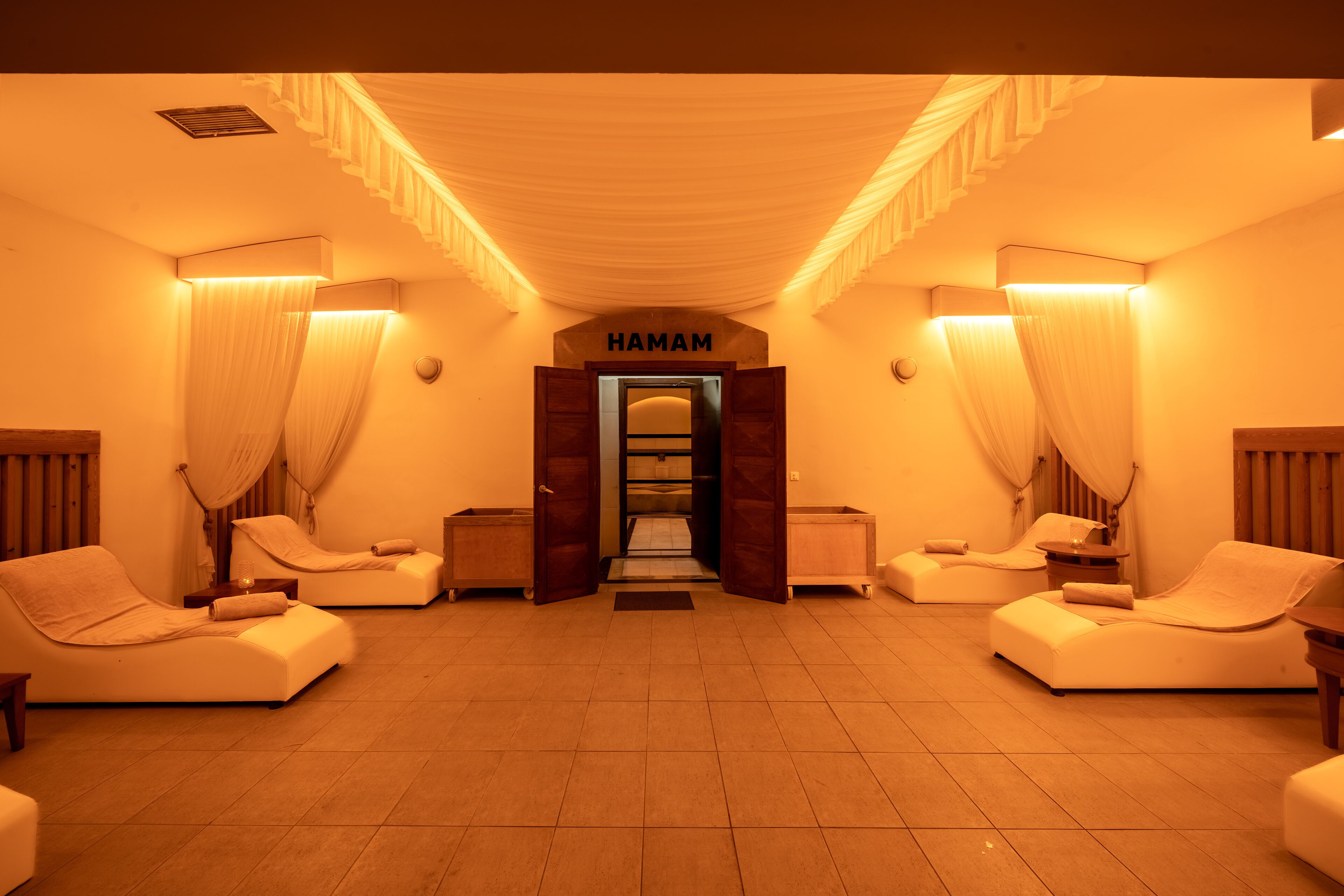 Une pièce avec deux fauteuils inclinables, une porte portant l’inscription « HAMAM » et un sol carrelé.