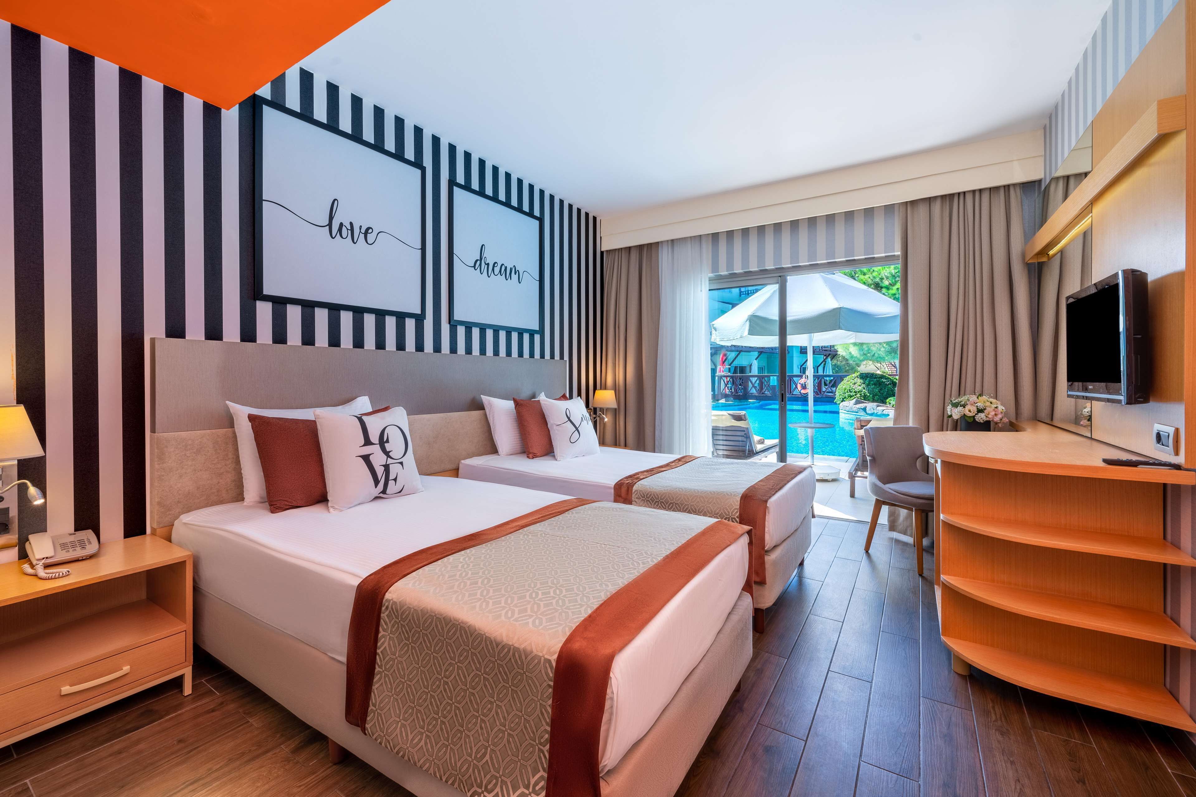 Une chambre d’hôtel avec deux lits, un bureau, une télévision et une vue sur la piscine.