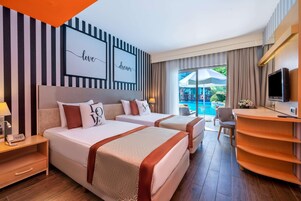Quarto de hotel com duas camas, uma mesa, uma televisão e vista para a piscina.