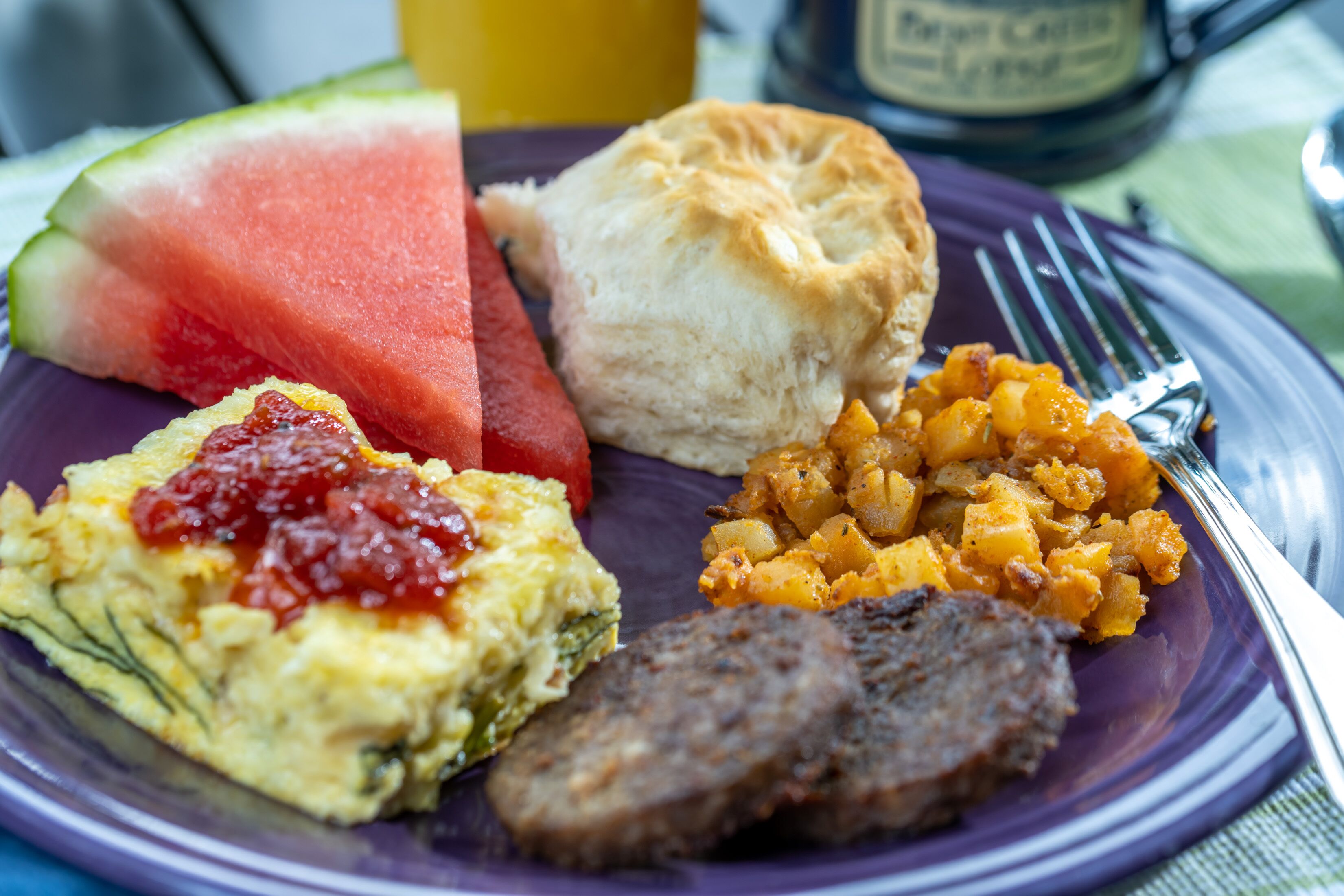 A plate with breakfast items including scrambled eggs, sausage, toast, and a slice of watermelon.