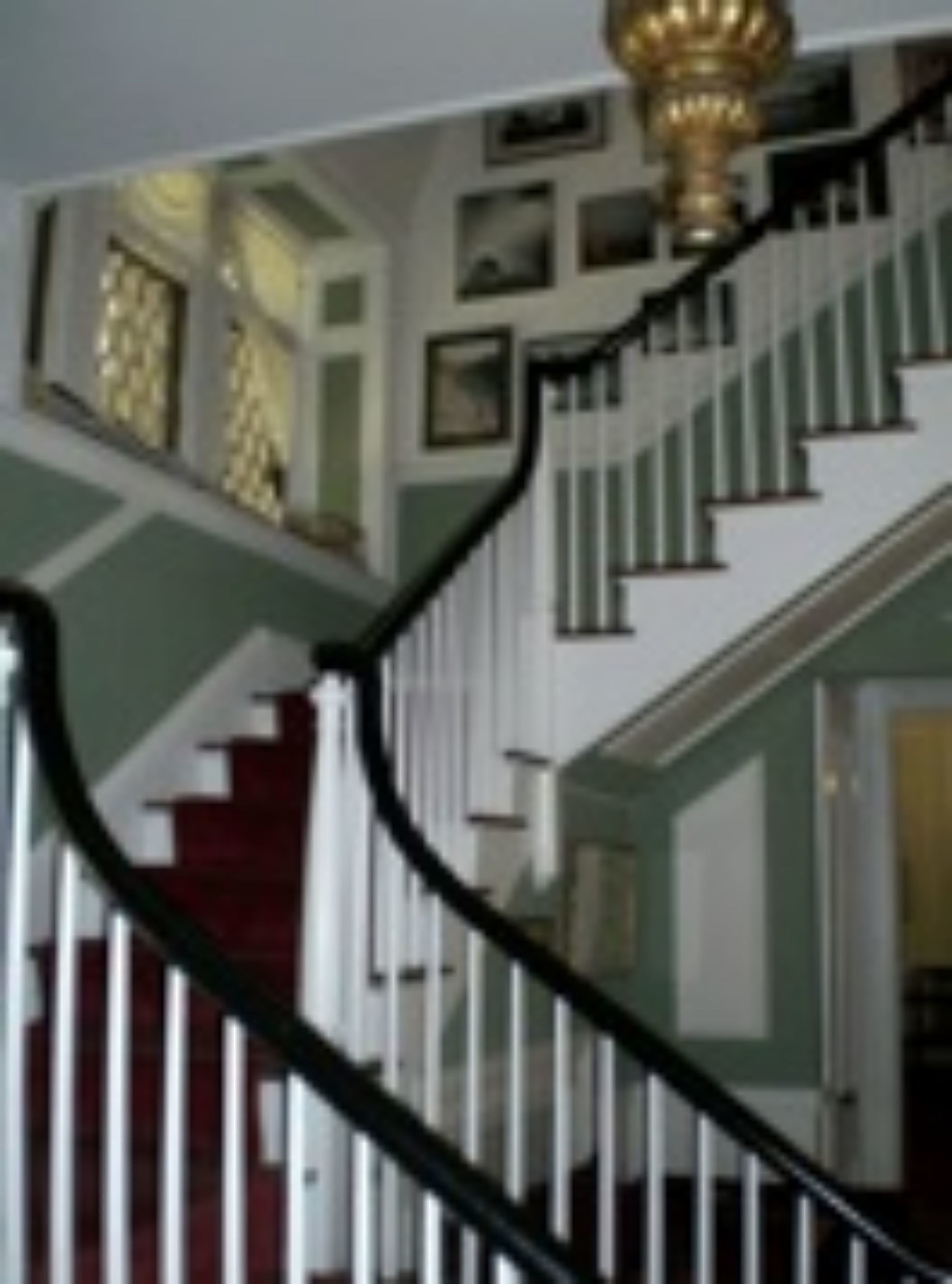 Eine prächtige Treppe mit schwarzer Handläufe, weißen Balustern und einer vergoldeten, aufwendig verzierten Balustrade.