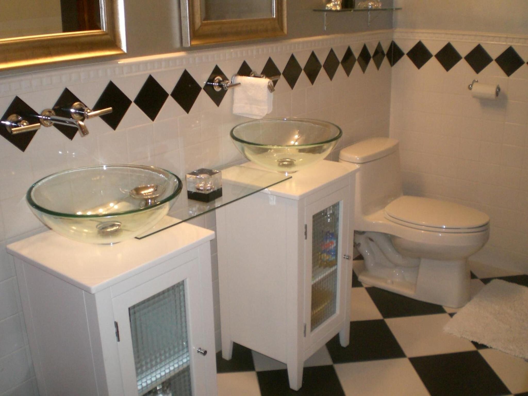 A bathroom with two glass sinks, a toilet, and a mirror above the sink.