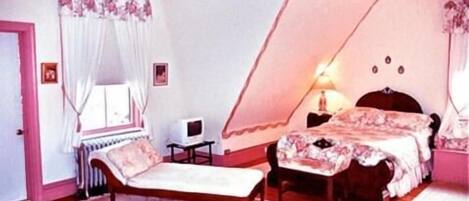 A bedroom with a bed, a chair, a bedside table, a lamp, and a window with curtains.