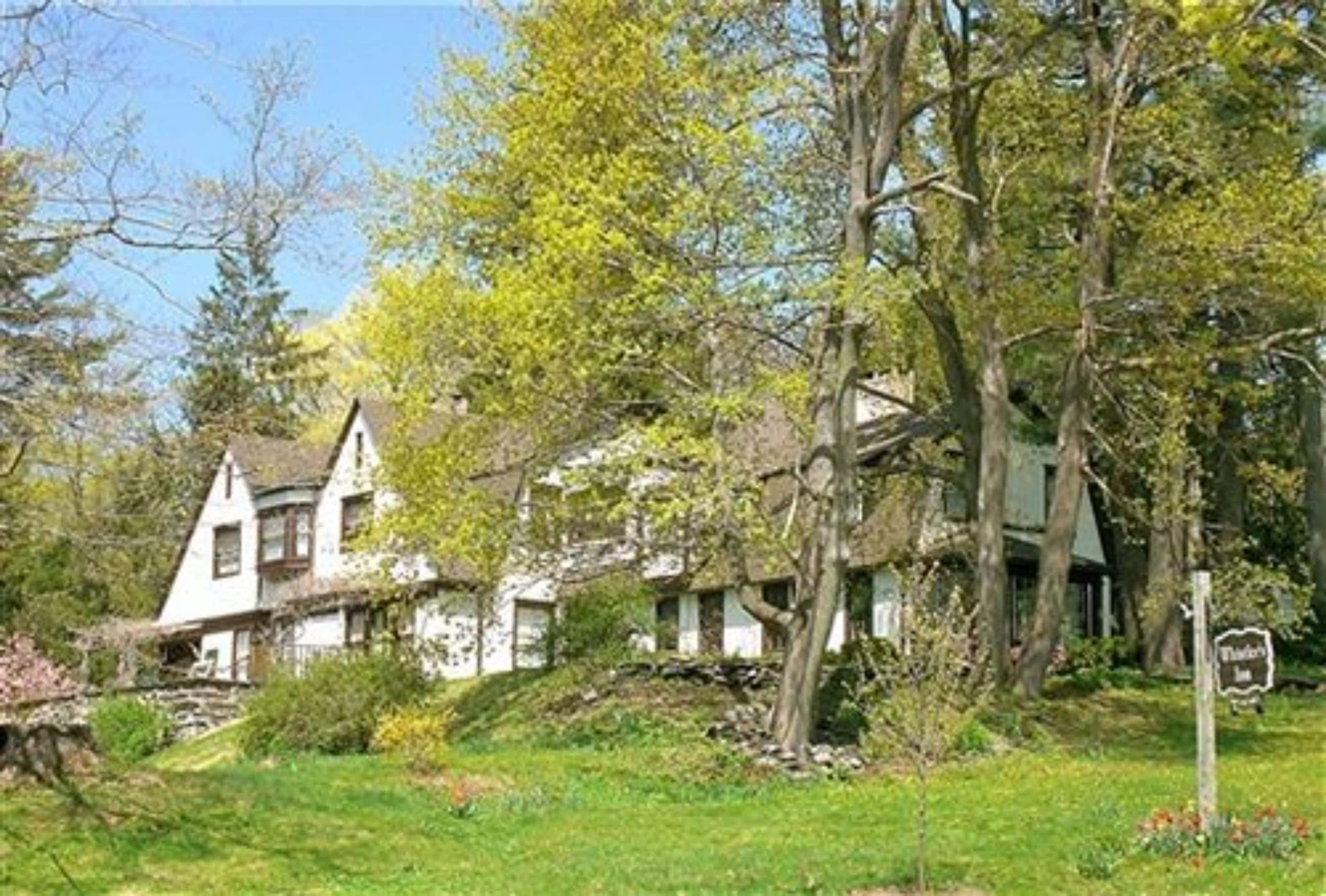 A traditional white building with a steeply pitched roof, surrounded by lush greenery and trees.