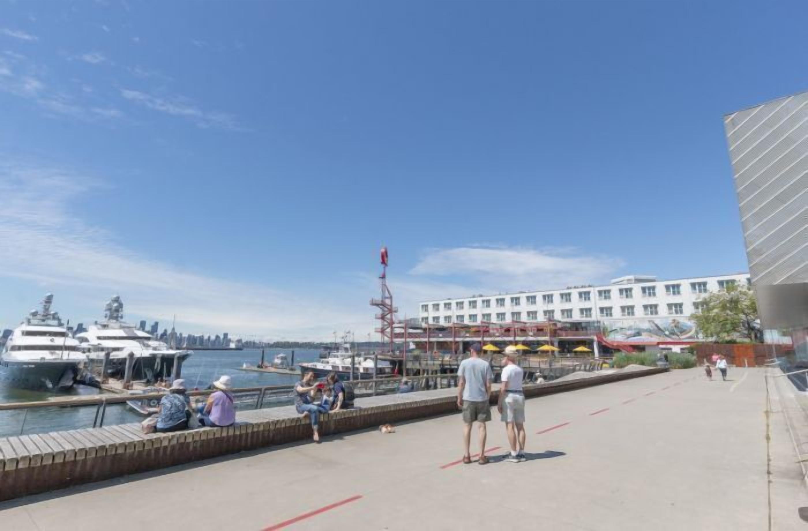 Un puerto deportivo frente al agua con yates amarrados, un edificio con varias ventanas y un paseo pavimentado.