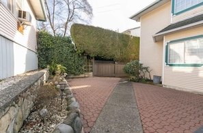 Un camino de entrada residencial con un muro de piedra, un seto y un sendero pavimentado que conduce a un portón de madera.