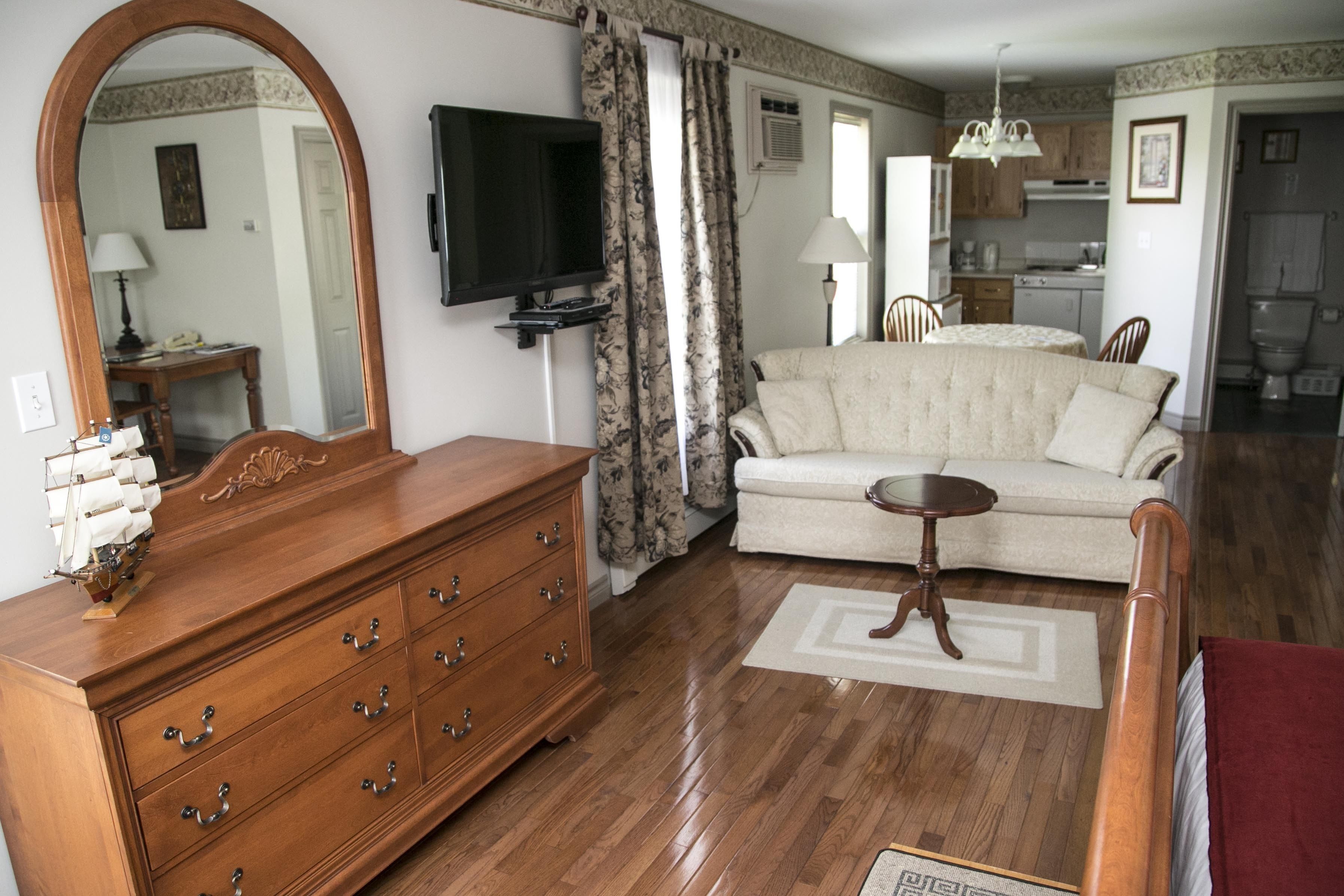 A living room with a wooden dresser, a sofa, a television, and a kitchen in the background.