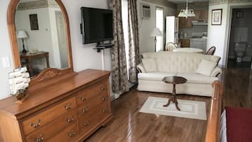 Un salon avec une commode en bois, un canapé, un téléviseur et, au fond, une cuisine.