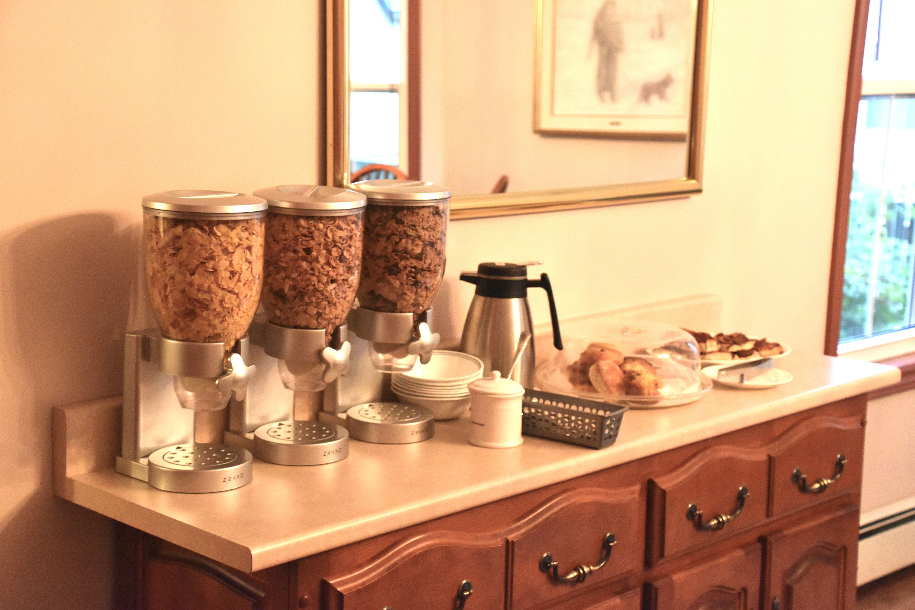 A kitchen counter with three coffee dispensers, a coffee pot, and a plate of pastries.